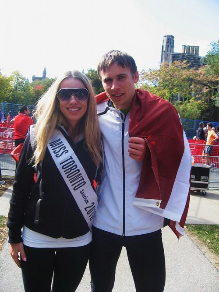 Ar valsts karogu plecos. Kurmenietis Jānis Arseņikovs Toronto maratonā izcīnīja augsto trešo vietu. Blakus Jānim — titula “Miss Toronto tourism 2010” ieguvēja.  Foto no Jāņa albuma