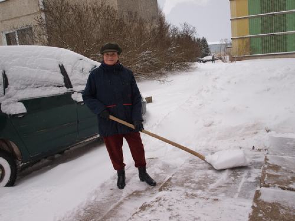 Emīlija Pance tīra sniegu pie daudzdzīvokļu mājas kāpņutelpas.