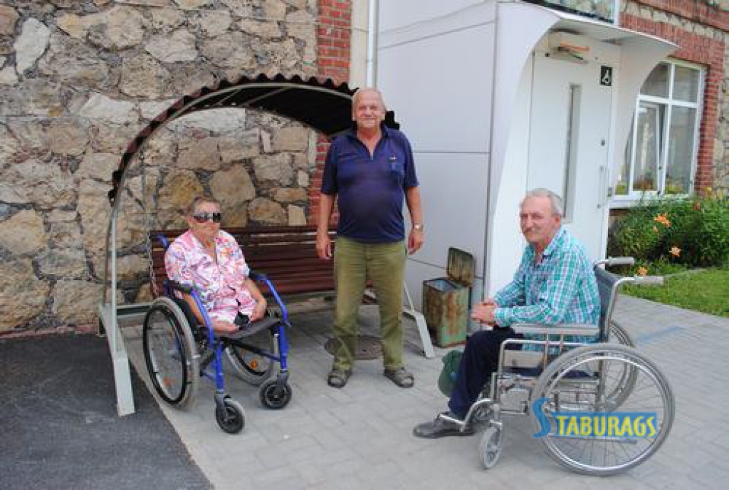 VIŅIEM TE PATĪK. “Prieks iznākt pagalmā!” saka aprūpes centra iemītnieki Silvija Vitkovska (no kreisās),  Pēteris Bogdāns un Antons Kazimirenoks. Aizmugurē —  šūpuļsols, kurā daudziem patīk sēdēt.