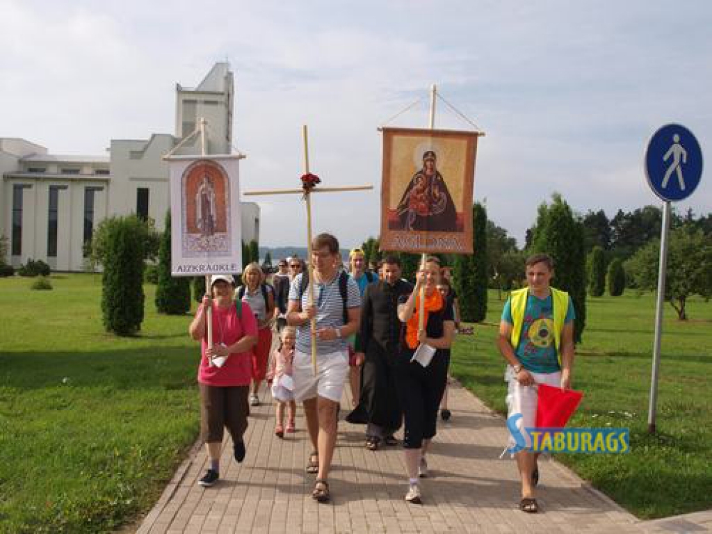 CEĻĀ UZ AGLONU. Pēc Svētās mises un lūgšanām vakar svētceļnieku grupa no Aizkraukles devās ceļā uz Aglonu. Krustu nes draudzes pārstāvis Edgars Prozorovskis, svētbildes posteru ar Aglonas vārdu — Baiba Fridrihsone no Alūksnes, bet posteru ar Aizkraukles nosaukumu — aizkraukliete Anita Trupa. Ejot pāri ceļam, satiksmi regulēs aizkrauklietis Kristiāns Hščanovičs (no labās). 