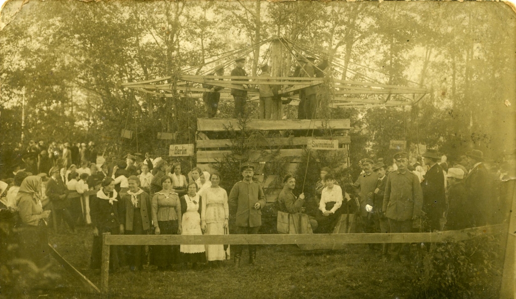Fotogrāfija ir labi saglabājusies, un tajā attēloti vasarīgi ģērbušies civilie, vīri formastērpos, kā arī interesants koka karuselis, kuru acīmredzot darbināja tā augšpusē esošie jaunieši. Vizināties gribētāji sēž no dēļiem veidotos, kamanām līdzīgos grozos, virs kuriem ir uzraksti ar dažādu pilsētu vārdiem.
Autors: no Aizkraukles Vēstures un mākslas muzeja arhīva