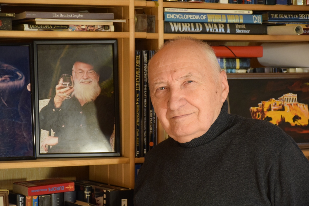 “Man ir pilnīgi visas viņa grāmatas. Oriģinālvalodā,” saka Edvards Lavrinovičs. Līdzās Edvardam — angļu rakstnieka, fantasta Terija Prečeta portrets.