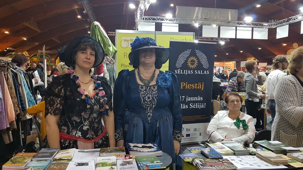 Ērberģes dāmas. Neretas novadu izstādē pārstāvēja Mazzalves pagasta pārvaldes vadītāja Zeltīte Odiņa (no kreisās) kopā ar pašvaldības izglītības un kultūras darba speciālisti Žannu Miezīti. Tērpušās viduslaikiem raksturīgās kleitās, viņas cita starpā piedāvāja uz vietas izkalt Ērberģes muižas laimes monētu. Tās vienā pusē attēlots barona Hāna dzimtas ģerboņa elements gailis, otrā — latvju raksti. Jaunajā tūrisma sezonā šādu monētu varēs sev izkalt katrs Mazzalves muižas apmeklētājs.