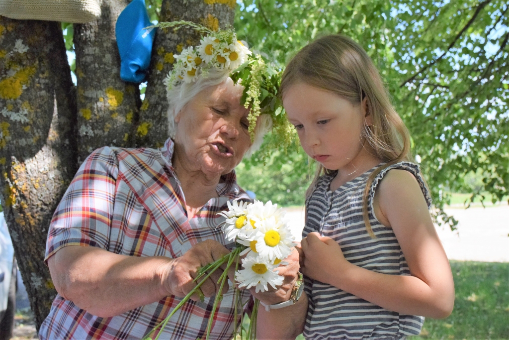 Koknesiete Ņina Rušmane mazajai Dārtai ierāda vainaga pīšanu, veidojot puķu bizīti.