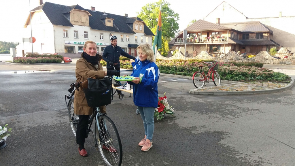 UZ DARBU AR VELOsipēdu cauri Pļaviņu “Velo vārtiem” dodas novada domes darbiniece Ineta Kaļva (no kreisās), kura saņem saldu pārsteigumu no Kristīnes Rulles. Šo pārvietošanās veidu izvēlējies arī pašvaldības vadītājs Aigars Lukss (aizmugurē).