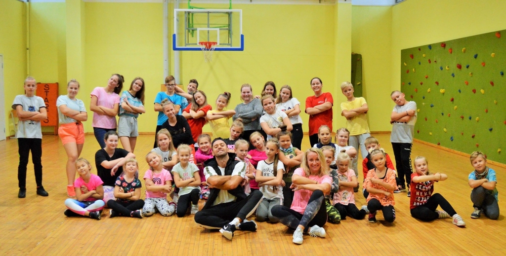 Pļaviņas. Gaidāmajos Latvijas Skolu jaunatnes dziesmu un deju svētkos, kas notiks nākamgad, jaunums būs mūsdienu deju grupu piedalīšanās šajā programmā. Tiem gatavojas arī Pļaviņu mūsdienu deju studija “Dancing Crystal” ar vadītāju Tatjanu Zagorsku. Dejotāji jau sākuši apgūt svētku programmas dejas, un saistībā ar to pie Pļaviņu dejotājiem ieradās deju treneris Alex Snikers, kurš ir Baltijā spēcīgākās ielu deju komandas “Jam Crew” dalībnieks, profesionāls treneris un starptautisku sacensību dalībnieks. Viņš būs arī skolēnu dziesmu un deju svētku horeogrāfs 1. — 4. klases grupai. Pļaviņiešiem viņš palīdzēja labāk apgūt deju un tās soļus, iedvesmojot tālākajam darbam. Sadarbība, visticamāk, turpināsies. 
Attēlā — azartiska nodarbība pļaviņiešiem izdevās kopā ar deju treneri Alex.
Autors: no deju studijas “Dancing Crystal”