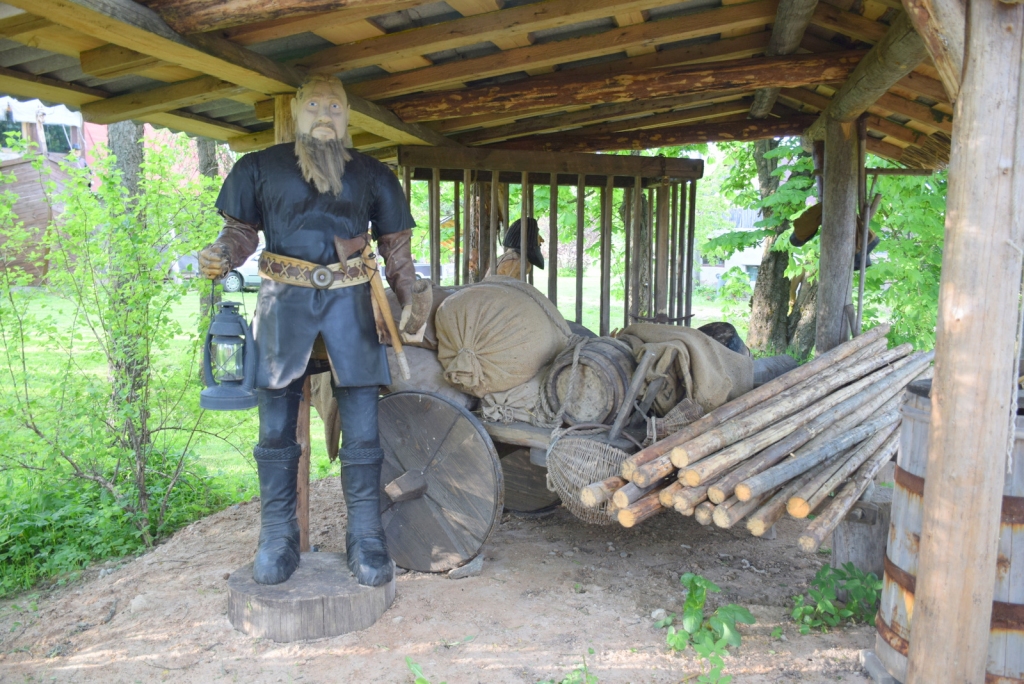 Sendienu tirgus laukumā. Fonā ratos — būris ar vergu.