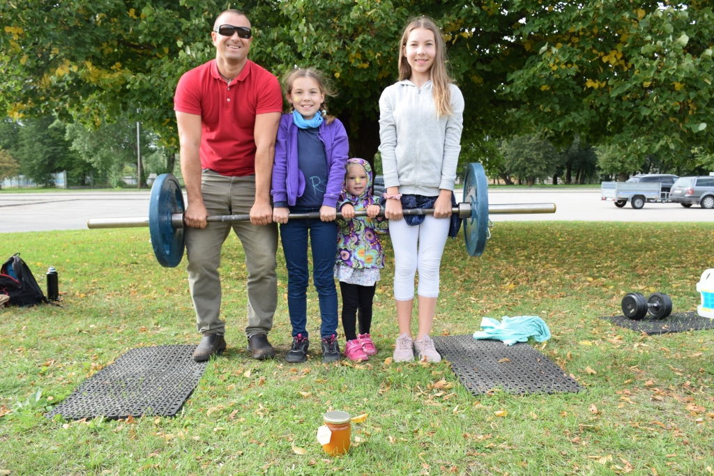 ATBRAUC SPECIĀLI NO RĪGAS. Kopvērtējumā 2. vietas ieguvējs Nauris Klētnieks šādu 60 kilogramus smagu svaru stieni sacensībās cēla viens pats, un ar savu klātbūtni viņam palīdzēja ģimene. Attēlā viņš stieni ceļ kopā ar  meitām — deviņus gadus veco Rūtu (no kreisās), trīsgadīgo Katrīnu un 13 gadus veco  Elīnu. “Informāciju par Tēva dienu Aizkrauklē uzzinājām portālā mammamuntetiem.lv un atbraucām no Rīgas speciāli uz šo pasākumu,” stāsta Nauris Klētnieks.