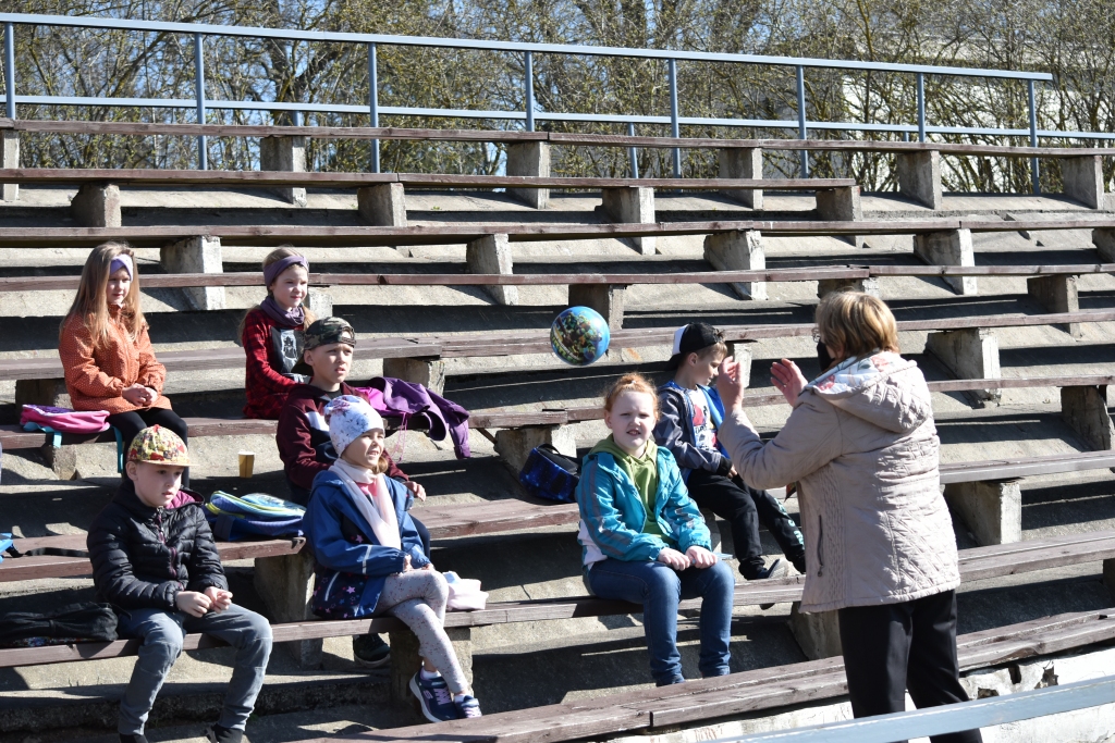 Jābūt radošam. Angļu valodas skolotāja Mārīte Kukīte kā diriģents nostājusies bērnu priekšā un vada stundu neierastā formā ārā — stadiona tribīnēs.