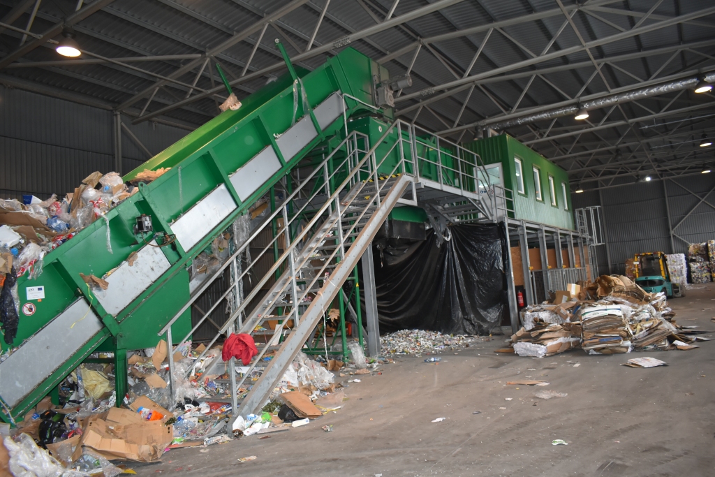 Šķirošanas līnija, kurā pa lenti tiek virzīti šķirotie atkritumi. Augšā darbinieki ar rokām tos sadala derīgajās kategorijās.