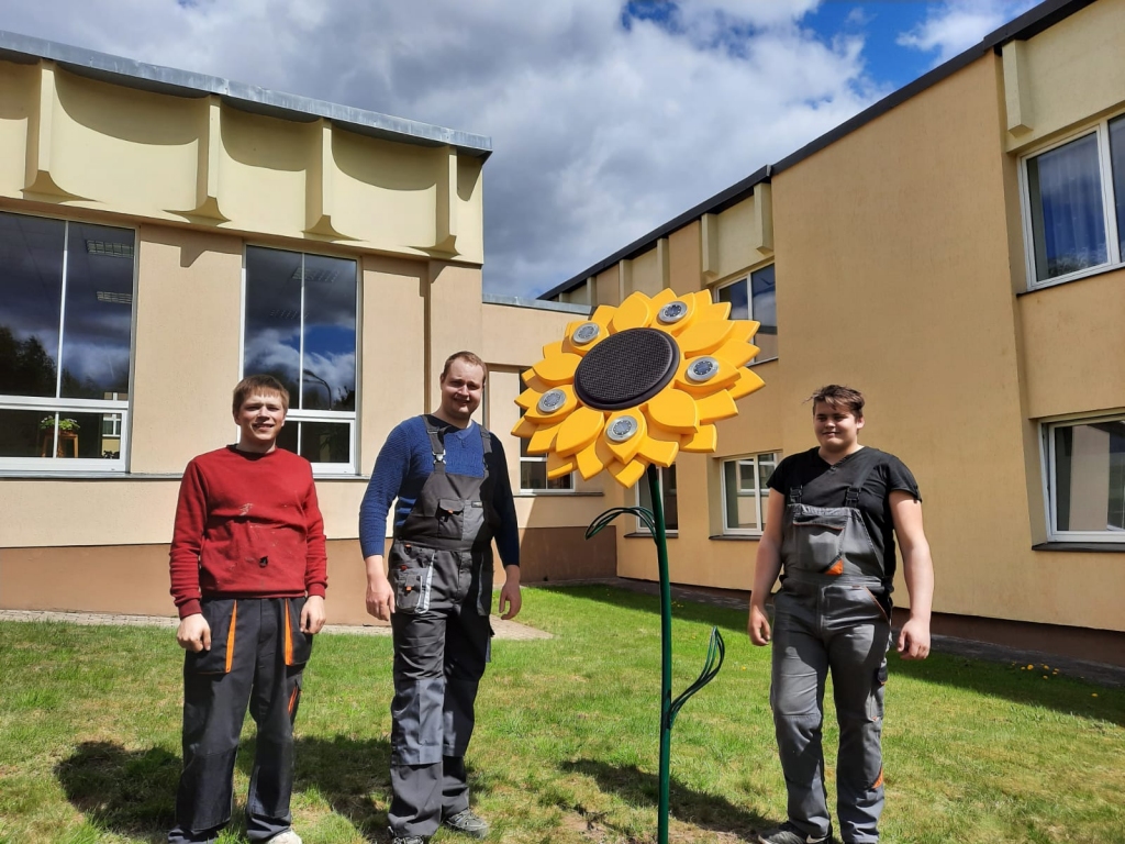 DARBS PABEIGTS! Jaunais vides objekts novietots netālu no skolas ieejas durvīm. Pie saulespuķes — topošie būvizstrādājumu galdnieki Niks Petrovs (no kreisās), Patriks Borovskis un skolotājs Jānis Madžulis (vidū).